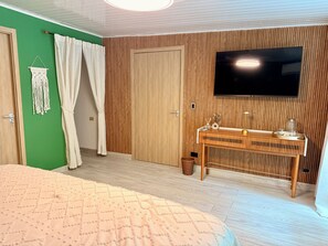 Una habitación con una cama, un televisor montado en la pared, un escritorio de madera y una pared de acento verde.
