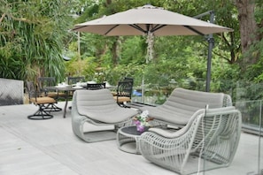 An outdoor seating area with wicker chairs and a table, surrounded by greenery.