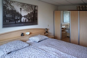 Ein Schlafzimmer mit einem Bett, einem Nachttisch, einer Wandlampe, einem Spiegel und einem großen Stadtbild.