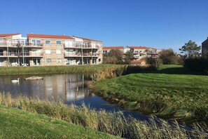 Ein Wohngebäude mit mehreren Balkonen, einem kleinen Teich und einer Rasenfläche.
