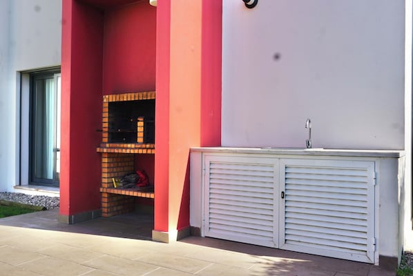 A building with a red and white exterior, a brick barbecue area, and a white garage door. - Spacious apartment for 2, near Baleal Beach (Ferrel, Peniche)