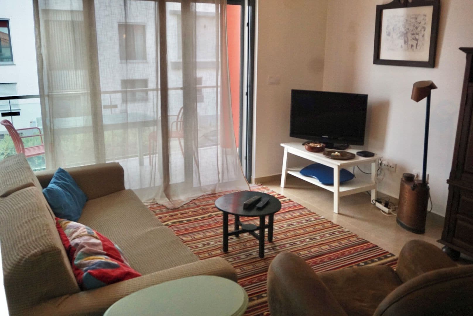 Una sala de estar con sofá, televisor sobre un mueble bajo, una mesa de centro y un tapete estampado.