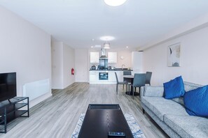 A modern living room with a flat-screen TV, a sofa with blue cushions, and a coffee table. - Spacious 2BDR with Modern Comfort Sleeps 4 (Manchester)
