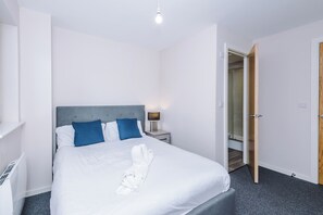 A hotel room with a bed, a nightstand, a lamp, and a door leading to a bathroom. - Spacious 2BDR with Modern Comfort Sleeps 4 (Manchester)
