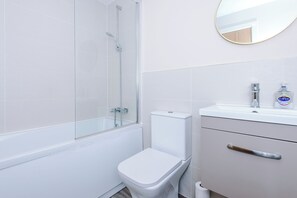 A bathroom with a glass-enclosed shower, a white toilet, a sink with a mirror, and a bottle of hand soap. - Spacious 2BDR with Modern Comfort Sleeps 4 (Manchester)