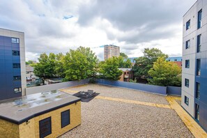Eine Dachterrasse mit Kiesboden, einem Grill und Blick auf umliegende Gebäude und Bäume.