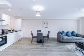 A modern kitchen with white cabinets, a dining area with a round table and chairs, and a grey sofa with blue cushions. - Spacious 2BDR with Modern Comfort Sleeps 4 (Manchester)
