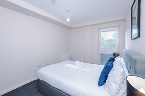 A hotel room with a bed, a window with blinds, a wall socket, and a ceiling light. - Spacious 2BDR with Modern Comfort Sleeps 4 (Manchester)