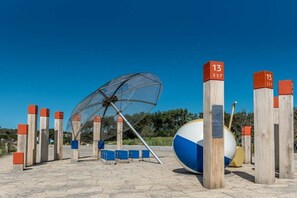 A beach with a large umbrella structure, wooden posts with numbers, and a beach ball. - Holiday home in Renesse with swimming pool (Renesse)