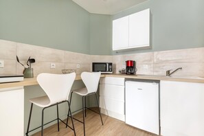 Una cocina moderna con gabinetes blancos, microondas, cafetera y dos taburetes de bar.