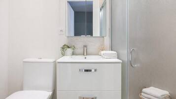 A modern bathroom with a toilet, sink, and mirror. There is a towel rack with folded towels and a small plant on the sink.