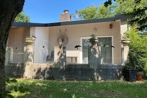 Een bakstenen huis met een schotelantenne, een raam met een decoratieve vogelsculptuur en een grote plantenbak met een vogelbeeldje.