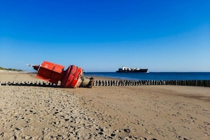Een strand met een rode boot en een schip op de achtergrond.