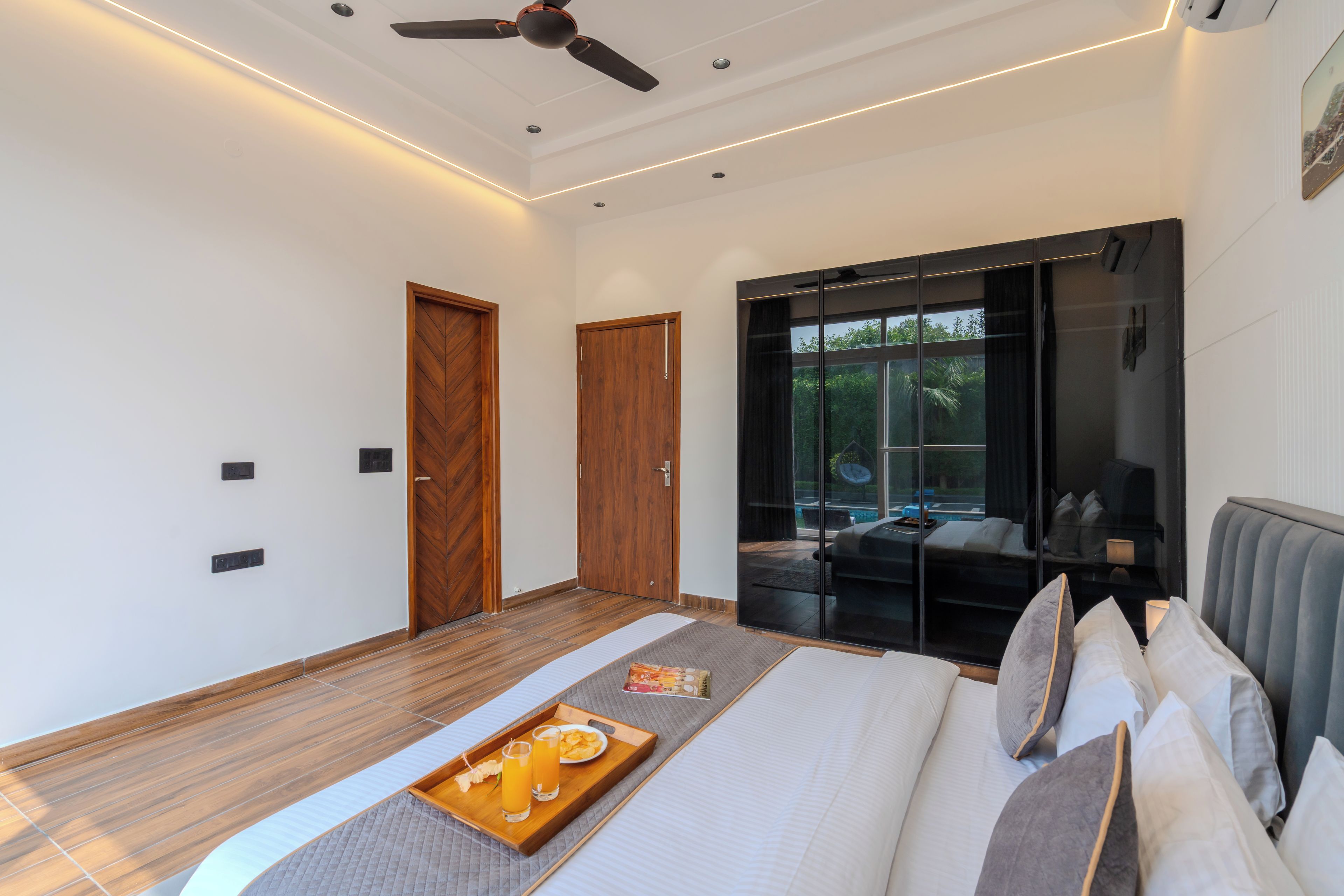 A modern bedroom with a bed, a tray with snacks, a ceiling fan, and a sliding glass door leading to a balcony.