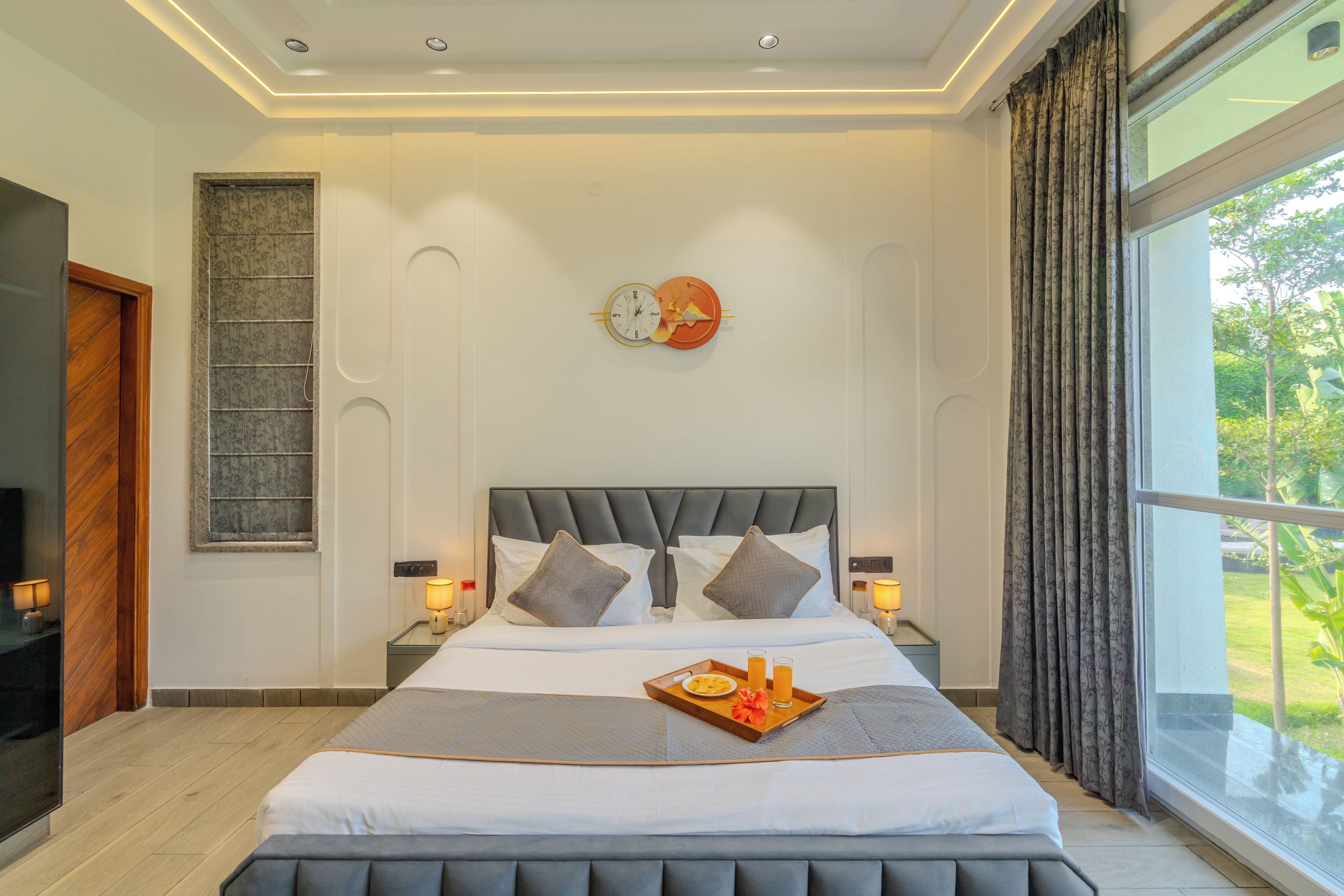 A modern bedroom with a large bed, two bedside lamps, a wall clock, and a window with curtains.