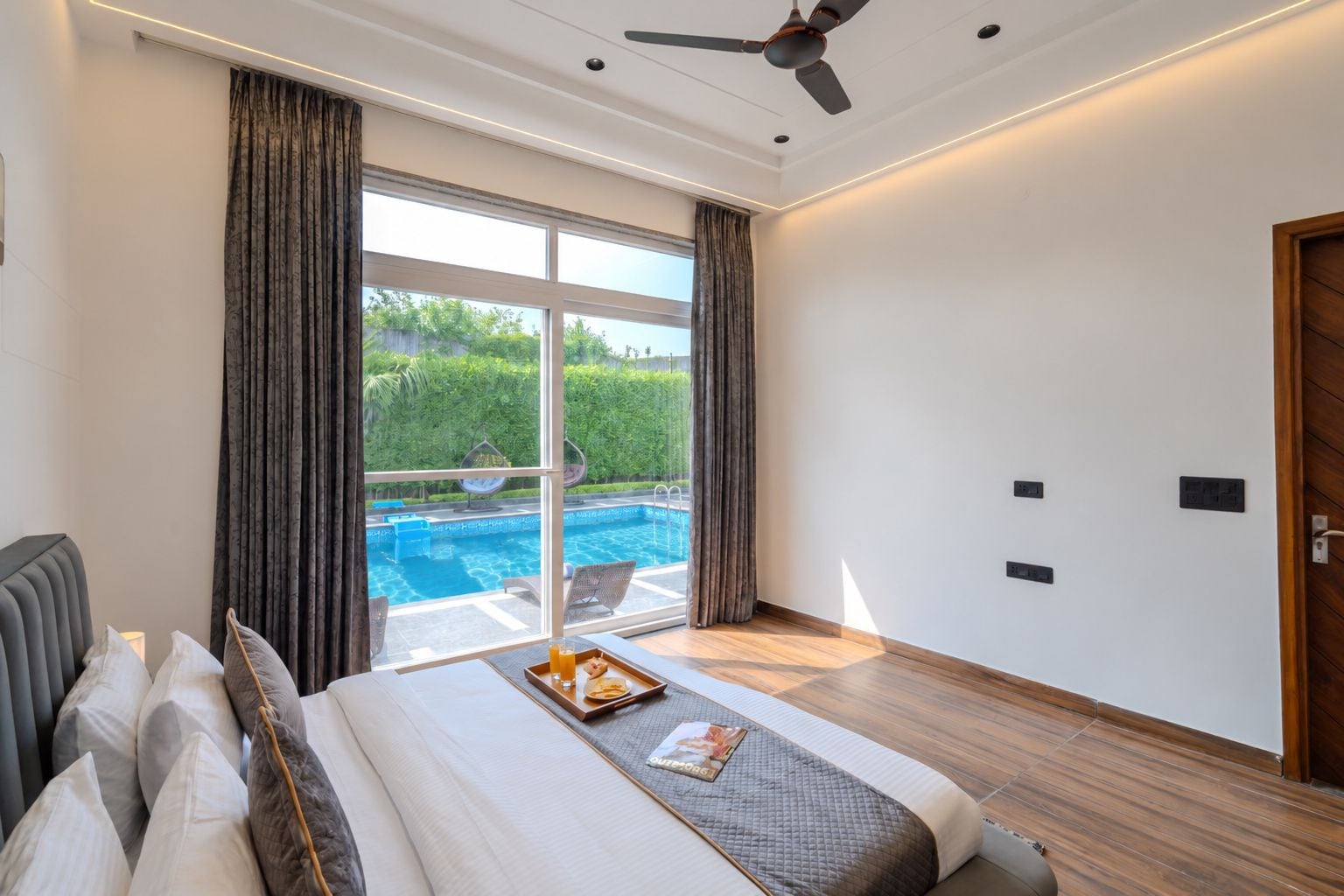 Une chambre avec un grand lit, un ventilateur de plafond, une vue sur une piscine et une porte sur le côté droit.