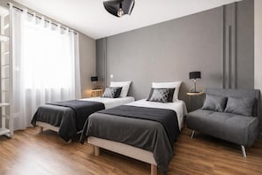 Una habitación de hotel moderna con dos camas, un sofá y piso de madera.