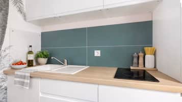A kitchen with a modern design, featuring a sink, a stove, and a countertop with a potted plant and kitchen essentials.