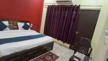 A bedroom with a bed, a dark-colored wardrobe, a small table with a water bottle, and a curtain.