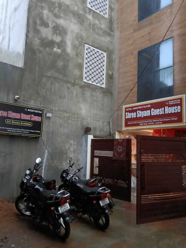 A guest house with a signboard, two motorcycles parked in front, and a gated entrance.