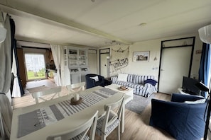 Un espacio habitable compacto con comedor, sofá, televisor y kitchenette.