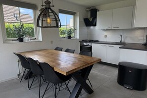 A modern kitchen with white cabinets, a wooden dining table, and black chairs. - Beach Parcel 207 in the Strandslag holiday park (Julianadorp)