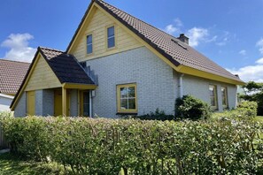 A two-story house with a gabled roof, a front porch, and a well-maintained garden. - Beach Parcel 207 in the Strandslag holiday park (Julianadorp)