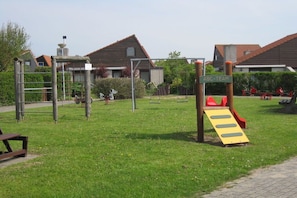 Een speeltuin met een glijbaan en klimtoestellen, omringd door een gazon en woongebouwen.