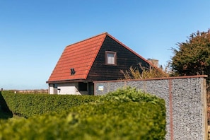 Un bâtiment d’un seul étage, avec un toit rouge, entouré d’une haie et d’une clôture en métal.