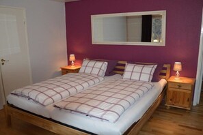 Un lit double avec une couvre-lit à carreaux, deux tables de chevet avec des lampes, un miroir au-dessus du lit et un plancher en bois.