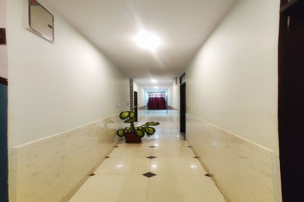 Un couloir avec une plante en pot, une porte au fond et un rideau rouge.
