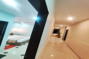 Un pasillo de hotel con una cama, un felpudo rojo y una planta en maceta.