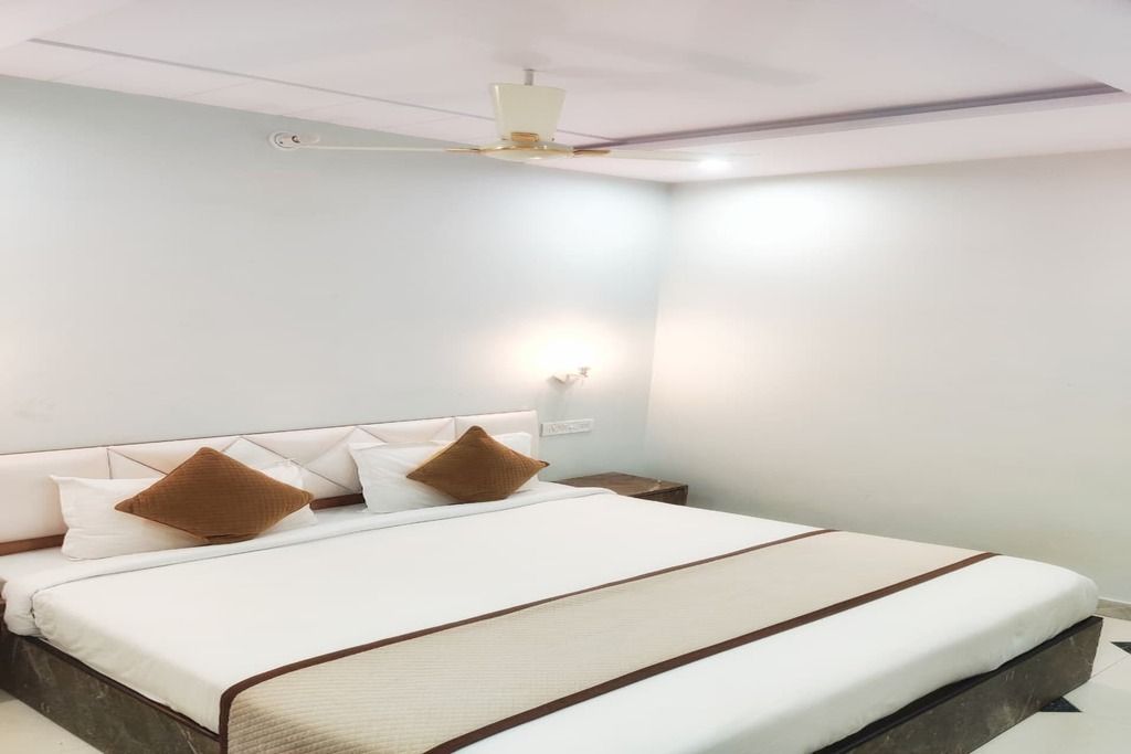 Une chambre d’hôtel avec un lit, une table de chevet, une lampe fixée au mur et un ventilateur de plafond.