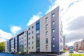 A modern multi-story residential building with a flat facade, numerous windows, and a parking area with cars. - Bright and Modern 2BDR 2BA Relaxing City Stay (Manchester)