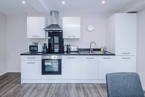 A modern kitchen with white cabinets, a stainless steel range hood, a built-in oven, and a sink. - Bright and Modern 2BDR 2BA Relaxing City Stay (Manchester)