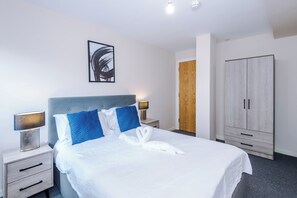 A hotel room with a bed, a nightstand, a lamp, a wardrobe, and a painting on the wall. - Bright and Modern 2BDR 2BA Relaxing City Stay (Manchester)