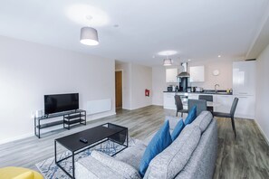 A modern living room with a flat-screen TV, a sofa with blue cushions, a coffee table, and a dining area with a kitchen in the background. - Bright and Modern 2BDR 2BA Relaxing City Stay (Manchester)
