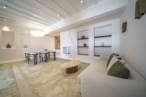 A modern living room with a white sofa, a round coffee table, and a dining area with chairs and a table. - Unparalleled luxury and warmth meet sweeping Aegean blues - The ultimate Mykonos retreat (Mykonos)