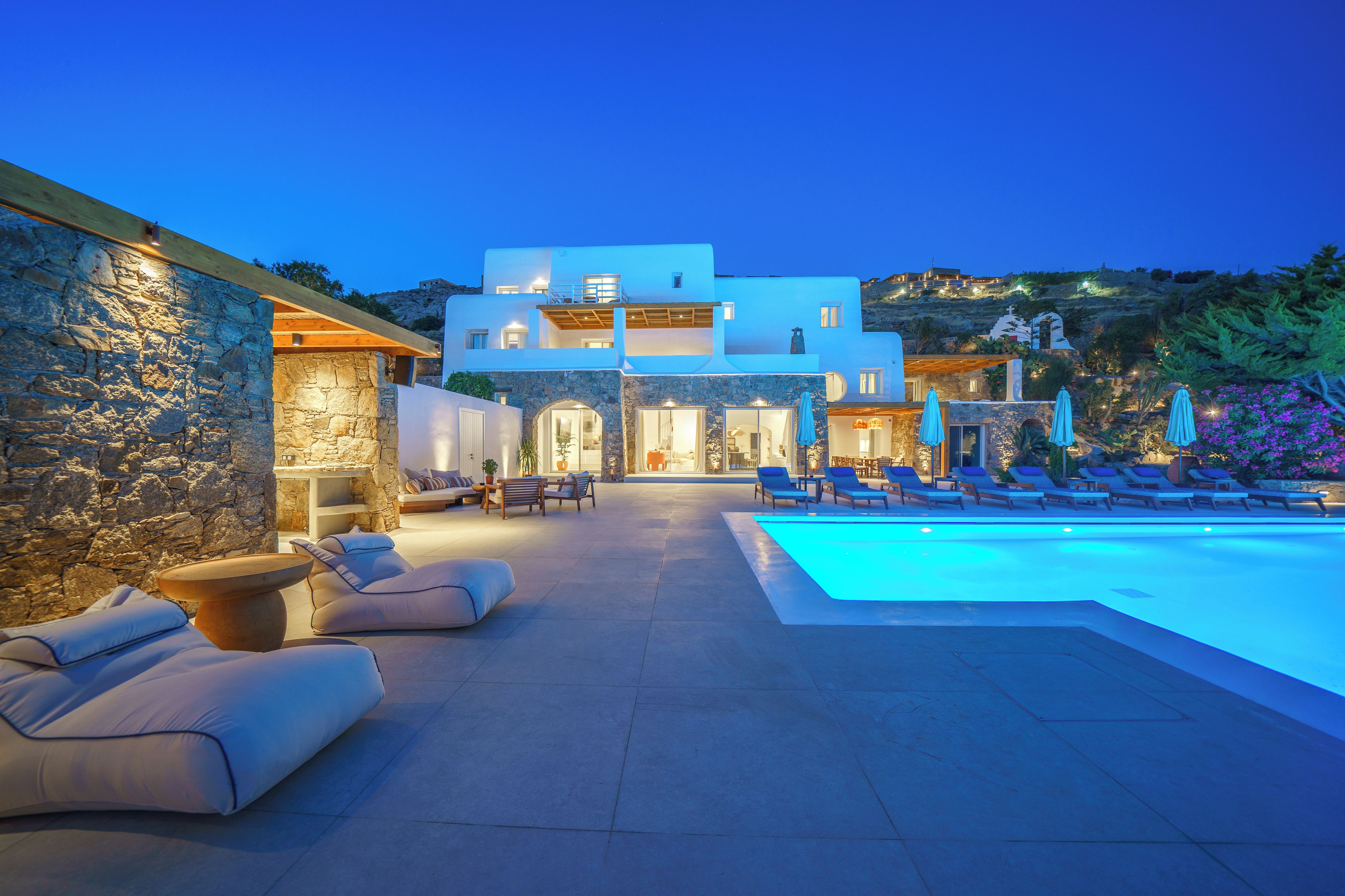A modern villa with a swimming pool, outdoor seating, and a stone wall.
