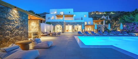 A modern villa with a swimming pool, outdoor seating, and a stone wall.