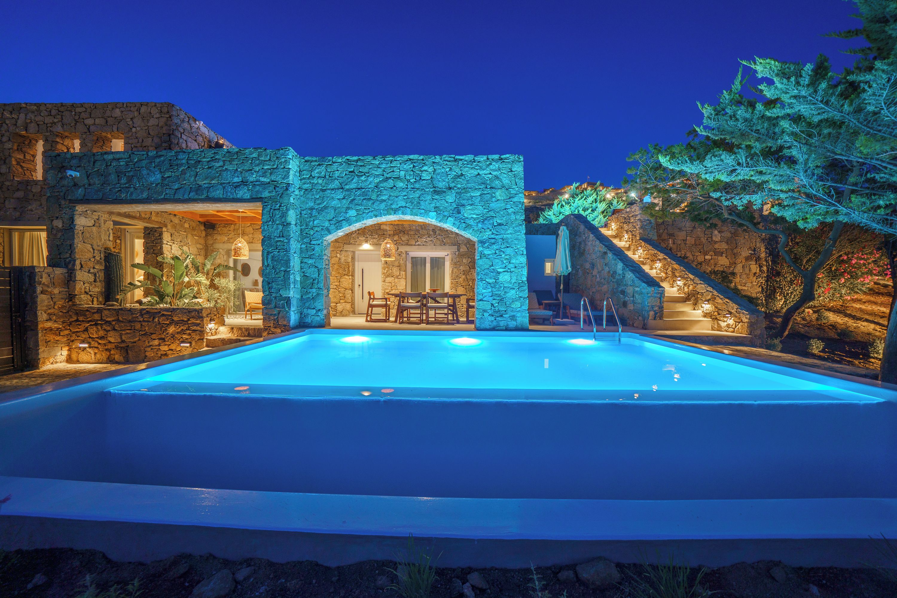 A poolside area with stone walls, a seating area, and a staircase leading to a higher level.