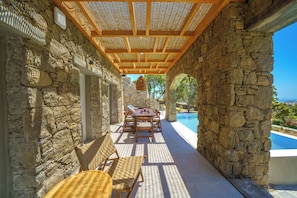 Ein Sitzbereich im Freien mit Steinsäulen, einem Pool, Holzmöbeln und einer Pergola darüber.