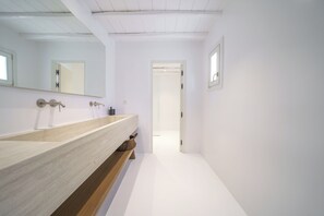 Un baño moderno con un mueble de tocador de madera, un espejo y una puerta que conduce a otra habitación.