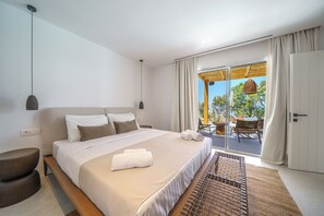 Een moderne hotelkamer met een groot bed, een klein bijzettafeltje en uitzicht op het buitengebied door een schuifdeur van glas.
