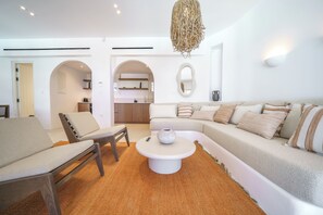 A modern living room with a sofa, chairs, a coffee table, and a kitchen in the background. - Secluded Cycladic serenity meets an endless blue horizon in Mykonos (Mykonos)