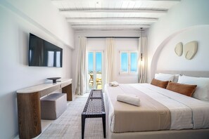Quarto de hotel moderno com cama, escrivaninha, um banco e televisão.