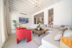 Uma sala de estar moderna com uma poltrona vermelha, um sofá e uma mesa de centro. Há um quadro grande na parede e um vaso com planta.