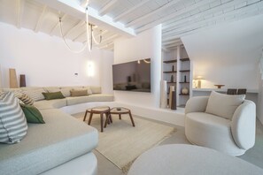 A modern living room with a sectional sofa, a round coffee table, and a TV mounted on the wall. - Unrivaled grandeur and absolute seclusion meet infinite Aegean horizons (Mykonos)