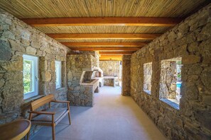 Corredor de paredes de pedra com vigas de madeira, um banco e lareira de pedra.