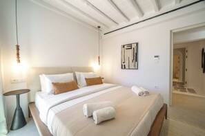 Une chambre d’hôtel comprenant un lit, des tables de chevet, une œuvre d’art accrochée au mur et une porte donnant sur une autre pièce.